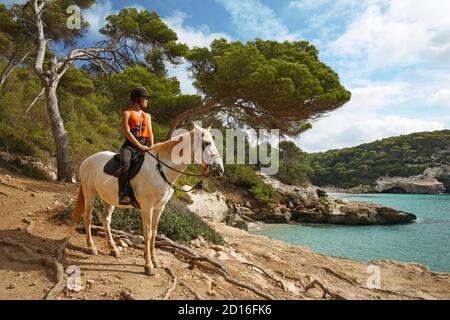 Spanien, Balearen, Menorca, cala Mitjan, junge Dame auf dem Pferderücken mit Blick auf einen wilden Bach in klarem Wasser gebadet und von Pinien umgeben Stockfoto