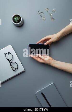 Oben Ansicht Hintergrund der weiblichen Hände halten Smartphone mit leerem Bildschirm, während der Arbeit an grauen Schreibtisch, kopieren Raum Stockfoto