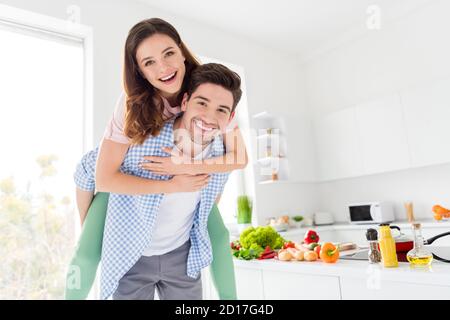 Portrait von seinem er sie sie zwei schöne attraktive positive Fröhlich fröhlich froh Ehegatten Vorbereitung hausgemachtes Abendessen mit Spaß Kerl Piggy-Backing Mädchen in Stockfoto