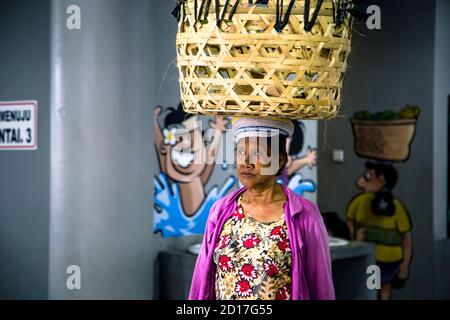 Denpasar, Bali, Indonesien - 8. AUGUST 2019 : neugieriges Porträt einer Frau, die einen Korb auf dem Kopf bringt. Stockfoto