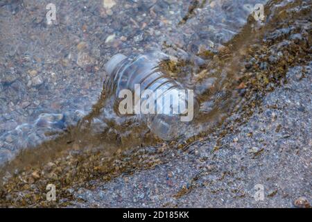 Eine weggeworfene Plastikflasche Müll weggeworfen auf Das Ufer fing in der Strömung auf dem felsigen Strand Die Umwelt verschmutzen Stockfoto