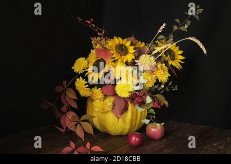 Blumenarrangement mit Sonnenblumen in einem Kürbis auf einem Holztisch auf schwarzem Hintergrund. Thanksgiving und Copy Space Konzept Stockfoto