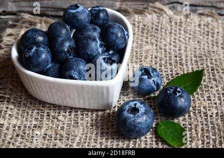 Frische Bio-Heidelbeeren in einer weißen herzförmigen Schale auf altem Holzhintergrund.Heidelbeere. Heidelbeeren.gesunde Ernährung, veganes Essen oder Diät-Konzept. Stockfoto