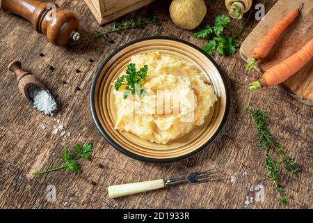 Pürierte Pastinaken mit Kartoffeln und Karotten und Zutaten für das leckere Pastinaken-Püree auf dunklem Holzhintergrund. Lecker und gesund vegetarisch Stockfoto