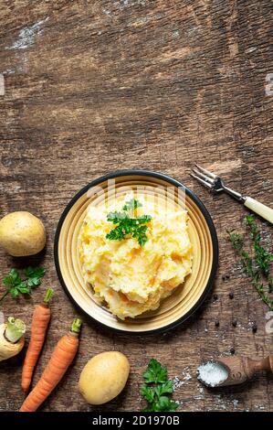 Pürierte Pastinaken mit Kartoffeln und Karotten und Zutaten für das leckere Pastinaken-Püree auf dunklem Holzhintergrund. Lecker und gesund vegetarisch Stockfoto