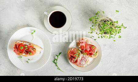 Italienisches Frühstück. Hausgemachte Sandwiches mit Prociutto crudo, Frischkäse, Mikrogemüse und Kaffee. Flach liegend Stockfoto