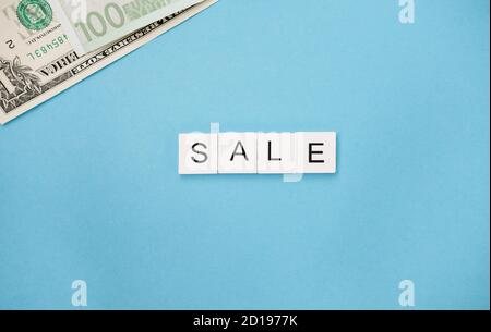 Die Word Sale sind in Holz Buchstaben Fliesen und Banknoten auf einem blauen trendigen Hintergrund geschrieben. Promotion saisonalen Angebot Anzeigen. Stockfoto