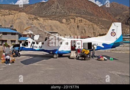 JOMSOM, NEPAL - 05. OKTOBER 2008: Passagiere kamen an und entluden Gepäck aus dem Flugzeug der Sita Airlines am Jomsom Flughafen, Annapurna Region Stockfoto