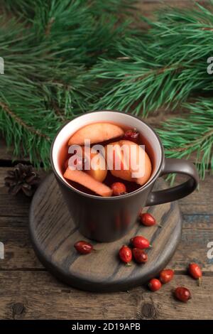Braune Tasse mit Glühwein, Beeren und Tannenzweigen auf dunklem Holzgrund. Stockfoto