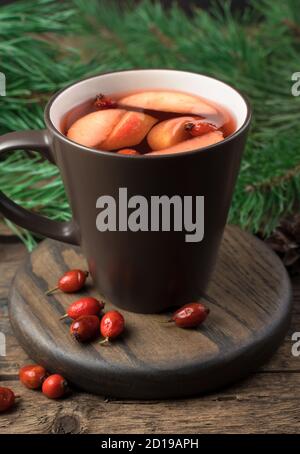 Früchtetee mit Äpfeln und Beeren, umgeben von Pinienzweigen auf dunklem Holzgrund. Stockfoto