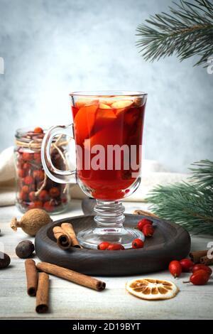 Neujahr trinken Glühwein umgeben von Gewürzen, Kiefernästen, Zimtstangen, roten Beeren und getrockneten Zitronen auf einem hölzernen Hintergrund. Stockfoto