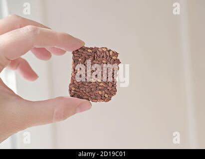 Hand hält knusprige Mehrkorngetreide Leinsamen Knäckebrot. Quadrate Bars für gesunde Snacks. Energie-Riegel ohne Zucker hinzugefügt. Stockfoto