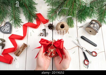 Weihnachtskonzept, menschliche Hände bereiten Weihnachtsspielzeug auf dem Hintergrund der roten Band, Schere und Tannenzweige. Stockfoto