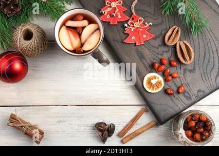 Eine Tasse Glühwein, Beeren und getrocknete Zitrusfrüchte, Zimtstangen, Tannenzweige und Spielzeug auf dem Brett Draufsicht. Stockfoto