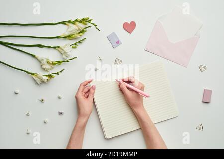 Minimale Hintergrundkomposition von weiblichen Händen schriftlich in Planer vor, während Tisch Hintergrund mit floralem Dekor, Kopierer Raum Stockfoto