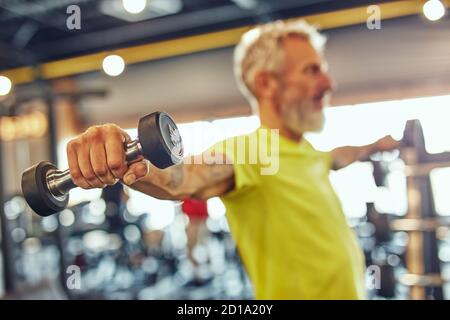 Mehr als fünfzig. Seitenansicht eines reifen kaukasischen Mannes beim Training mit Hanteln im Fitnessstudio, Fokus auf der Hand Stockfoto