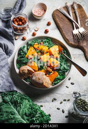 Salat mit gegrilltem Kürbis, Grünkohl, Kichererbsen, Pepitas und Nüssen würzen. Herbst vegetarisch gesundes Rezept. Stockfoto