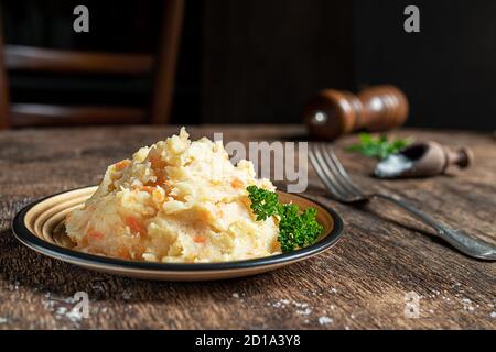 Kartoffelpüree mit Kartoffeln und Karotten auf dunklem Holzhintergrund in Nahaufnahme. Köstliche und gesunde vegetarische Lebensmittel, reich an Vitaminen und Mineralstoffen. Stockfoto