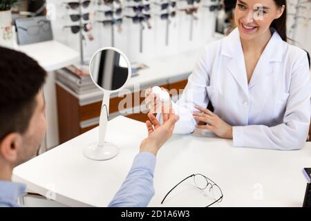 Optiker, der dem Patienten eine Plastikhülle mit Kontaktlinsen gibt Stockfoto