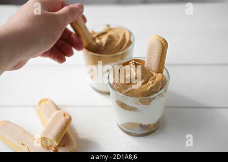 Iced schaumig Dalgona Kaffee Tiramisu, trendy flauschig cremig Schlagkaffee Dessert. Frau nimmt Schlagsahne mit Keks. Tiramisu mit koreanischen Getränk. Latte Espresso Dessert mit Kaffee Schaum. Stockfoto