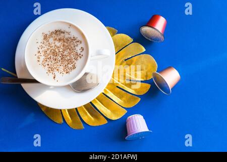 Tasse Espresso Kaffee, Cappuccino serviert mit Schoten und Kapseln auf blauem Tisch.Kaffeemaschine, bunte Kaffeekapseln. Guten Morgen heiße Getränke. Kopieren Stockfoto
