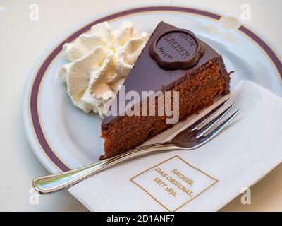WIEN, ÖSTERREICH - 14. JULI 2019: Stück Sacher-Torte-Torte-Torte auf Teller im Cafe Sacher mit gebrandeter Serviette und Gabel Stockfoto