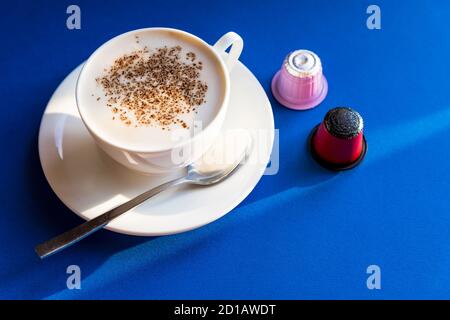 Tasse Espresso Kaffee, Cappuccino serviert mit Schoten und Kapseln auf blauem Tisch.Kaffeemaschine, bunte Kaffeekapseln. Guten Morgen heiße Getränke. Kopieren Stockfoto