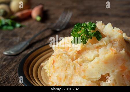 Kartoffelpüree mit Kartoffeln und Karotten auf dunklem Holzhintergrund in Nahaufnahme. Leckeres und gesundes vegetarisches Püree, reich an Vitaminen und Mineralstoffen. Stockfoto