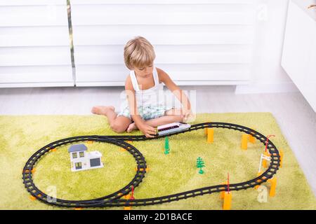 Kleiner Junge spielt mit Plastikeisenbahn. Kind mit Spielzeugzug. Pädagogisches Spielzeug für kleine Kinder. Kleiner Junge baut Eisenbahnschienen auf grünem Teppich. Stockfoto