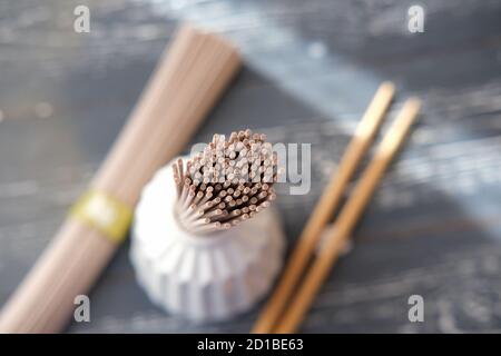 Trockene Soba-Nudeln und Essstäbchen auf grauem Tisch. Selektiver Fokus. Rohe Nudeln oder Buchweizen-Pasta. Braune japanische Pasta. Gesunde asiatische Art Essen. Stockfoto