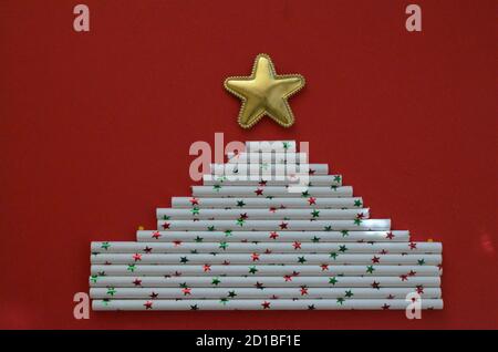 Minimalkonzept: Ein Weihnachtsbaum aus Trinkhalmen mit goldenem Stern auf rotem Hintergrund Stockfoto