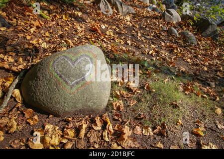 Wir lieben Herbst / Herbst. Der bemalte Stein mit Herz Symbol in der herbstlichen Natur, umgeben von getrockneten Orangenblättern. Stockfoto