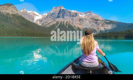 Emerald Lake Kanusport. Der Blick auf den Rücken der blonden Frau in rosa Spitze paddeln im Kanu auf dem schönen türkisfarbenen See. Der Berg und der Wald in