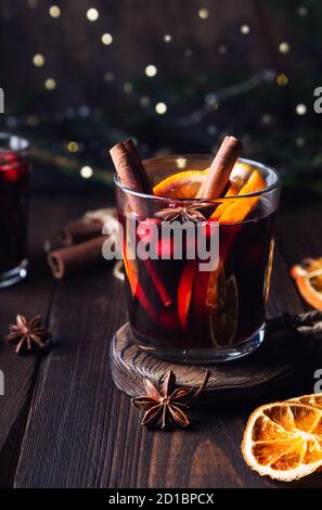 Weihnachtlicher Glühwein mit Preiselbeeren, Orange und Gewürzen auf rustikalem Holzhintergrund. Traditionelles warmes Getränk im Winter. Stockfoto