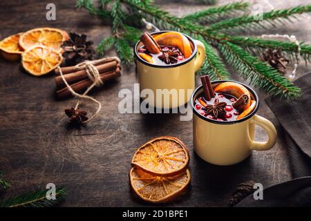 Weihnachts Glühwein mit Preiselbeeren, Orange und Gewürzen in Tassen auf rustikalem Sperrholz Hintergrund. Traditionelles warmes Getränk im Winter. Stockfoto