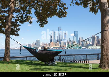 Genießen Sie die Aussicht auf die Skyline von New York City/Manhattan von der anderen Seite des Hudson River in Hoboken, New Jerseys Uferpromenade. Stockfoto