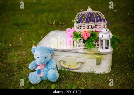 Straßendekorationen für eine Kinderparty. Retro Koffer mit Blumen mit einem Teddybären in einem grünen Park. Party auf der Straße. Stockfoto