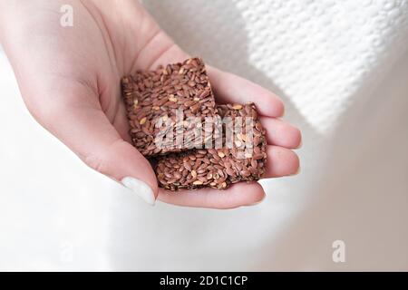 Hand hält knusprige Mehrkorngetreide Leinsamen Knäckebrot. Quadrate Bars für gesunde Snacks. Energie-Riegel ohne Zucker hinzugefügt. Nahaufnahme Stockfoto