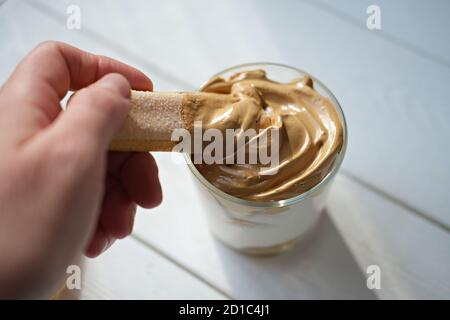 Iced schaumig Dalgona Kaffee Tiramisu, eine trendige flauschige cremige Kaffee-Dessert. Frau nimmt Schlagsahne mit Keks. Tiramisu mit koreanischem Getränk. Latte Espresso Dessert mit Kaffee-Schaum. Stockfoto