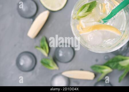 Zutaten für Mojito auf grauem Hintergrund. Limette, Zitrone, Minzblätter und hohes Glas mit Eiswürfeln. Sommer alkoholfreier Cocktail. Draufsicht Stockfoto