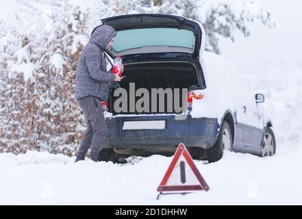 Mann, der eine Flasche Frostschutzmittel vor dem Gepäck eines beschädigten Autos hält. Stockfoto