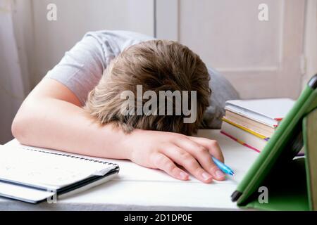 Müde Junge auf der Tischplatte liegen. Lern- und Prüfungskonzept. Junge mit pc-Tablet und Schulbücher schläft ein. Aufgeregt mit Hausaufgaben Schüler. Stockfoto