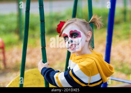 Ein kleines Mädchen mit gemaltem Gesicht zeigt lustige Gesichter am mexikanischen Tag der Toten. Stockfoto