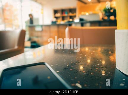 Moderne, verschwommene Café-Szene. Telefon und Kaffeetasse auf dem Tisch als Vordergrund. Weich verschwommener Sofastuhl, Bar / Theke Regale und Fenster vorne in der Stockfoto