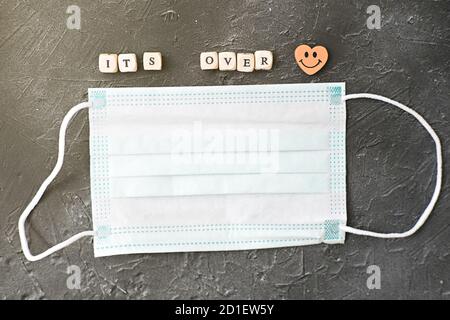 Quarantäne ist vorbei Zuschreibung. Ende der Quarantäne-Konzept. Medizinische Gesichtsmaske und Buchstaben auf Würfel über grauem Hintergrund. Zurück zum normalen Leben nach Coronavirus Pandemie. Draufsicht Stockfoto