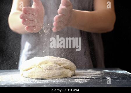 Teig von Hand in der Bäckerei oder zu Hause machen. Mehlwolke in der Luft. Nahaufnahme der Frau Chef Hände Vorbereitung für Kneten des Teiges auf dem Tisch, Pulver mit Mehl. Teig für Brot, Pasta oder Pizza Stockfoto
