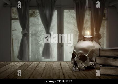 Stapel des Buches mit einem menschlichen Schädel und Kerze Auf einem Holztisch in einem verlassenen Haus Stockfoto