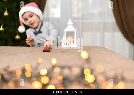 Ein Junge in einer gestreiften Mütze spielt Geschenke in der Nähe eines Weihnachtsbaums. Stockfoto