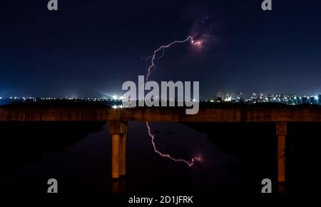 Gewitter mit Spiegelung des Blitzes über der Stadt Braut. Blitzschlag während eines Gewitters auf Metropolstadt. Dunkler Himmel mit Rand Stockfoto