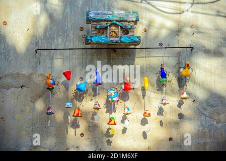 Ein kleines Vogelhaus aus Holz an einer Betonwand mit niedlichen und bunten Keramikfiguren Windspiele hingen darunter. Stockfoto